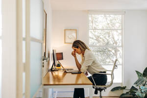 Erschöpfte Geschäftsfrau mit Kopfschmerzen in ihrem Büro. Überarbeitete Geschäftsfrau mit Arbeitsmüdigkeit, während sie vor einem Laptop sitzt. - JLPSF07286