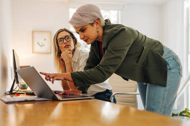 Young businesswoman collaborating with her colleague in a modern office. Confident young businesswoman using a laptop while working with her colleague in a woman-owned company. - JLPSF07294