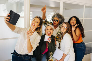 Multicultural businesspeople smiling happily while taking a selfie together in a creative office. Group of cheerful businesspeople celebrating their success on social media. - JLPSF07309