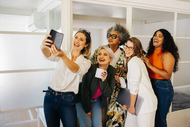 Diverse businesspeople smiling cheerfully while taking a selfie together in a creative office. Group of multicultural businesspeople celebrating their success on social media. - JLPSF07310