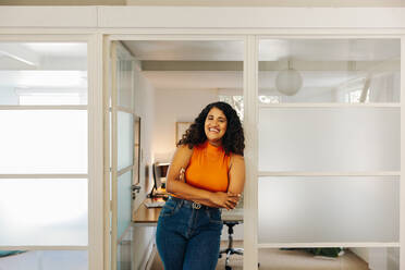 Happy young businesswoman smiling at the camera while standing in front of her office. Successful female entrepreneur working in a creative workplace. - JLPSF07328