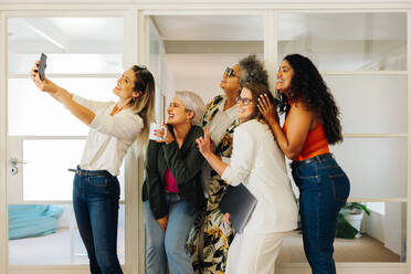 Multicultural businesspeople smiling cheerfully while taking a selfie together in a creative office. Group of happy businesspeople celebrating their success on social media. - JLPSF07331