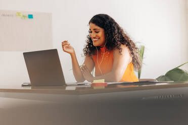 Glückliche junge Geschäftsfrau, die während eines Online-Meetings mit ihren Geschäftspartnern fröhlich lächelt. Erfolgreiche Geschäftsfrau, die einen Videoanruf in einem kreativen Büro führt. - JLPSF07338