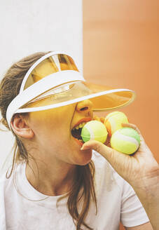 Sportlerin mit Sonnenblende beißt in Tennisball - SVCF00182