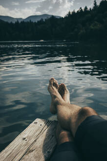Mann mit gekreuzten Beinen entspannt sich auf einem Steg am Monticolo-See - DMGF00876