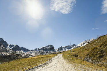 Dirt road leading towards snowcapped mountains on sunny day - ACPF01494