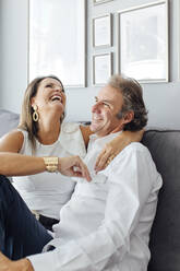 Woman with arm around man laughing on sofa in living room at home - EGHF00573