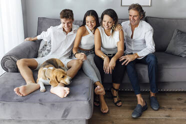Lächelnde Eltern und Kinder betrachten den Hund auf dem Sofa im Wohnzimmer zu Hause - EGHF00574