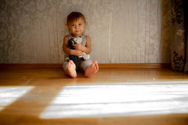 Niedlicher Junge mit Kuscheltier sitzt vor der Wand zu Hause - ANAF00178