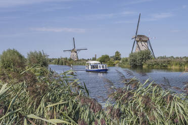 Niederlande, Südholland, Kinderdijk, Fluss auf dem Lande mit historischen Windmühlen im Hintergrund - KEBF02405