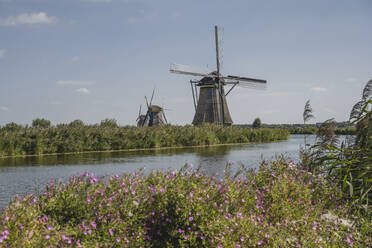 Niederlande, Südholland, Kinderdijk, Fluss auf dem Lande mit historischen Windmühlen im Hintergrund - KEBF02407