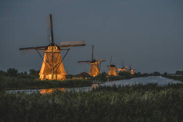 Niederlande, Südholland, Kinderdijk, Fluss auf dem Lande und historische Windmühlen bei Nacht - KEBF02418