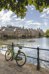 Netherlands, South Holland, The Hague, Bicycle leaning on railing of bridge stretching over Hofvijver lake canal with Binnenhof government office in background - KEBF02429