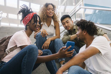 Woman sharing mobile phone with multiracial friends on staircase - MMPF00334