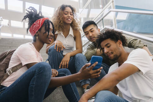 Gemischtrassige Freunde schauen am Bahnhof auf ihr Smartphone - MMPF00335