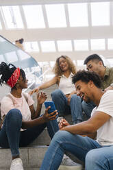 Multiracial friends watching smart phone and laughing on staircase - MMPF00337
