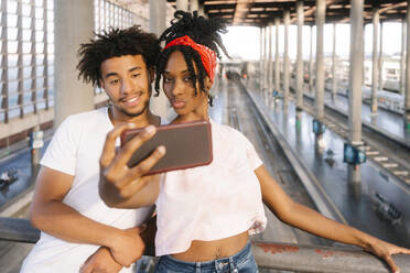 Gemischtrassige Freunde machen ein Selfie mit dem Handy am Bahnhof - MMPF00345