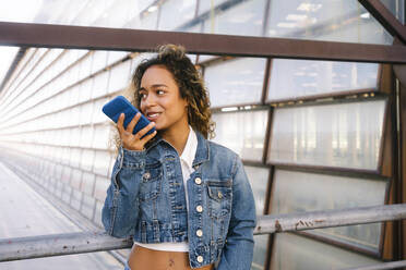 Junge Frau, die an einem Geländer mit ihrem Smartphone telefoniert - MMPF00349