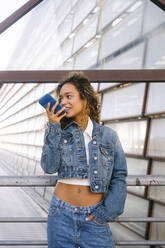 Young woman in denim jacket sending voicemail though smart phone - MMPF00350