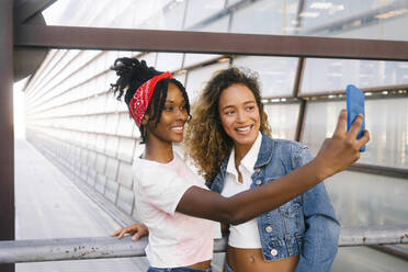 Lächelnde multirassische Frauen, die ein Selfie mit ihrem Handy am Geländer machen - MMPF00353