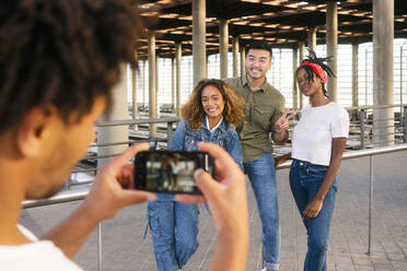 Man photographing multiracial friends posing at railroad station - MMPF00359