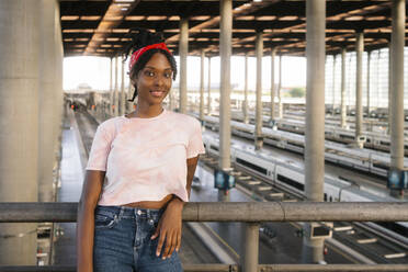 Smiling young woman leaning on railing at railroad station - MMPF00361