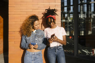 Young woman showing mobile phone to friend on sunny day - MMPF00364