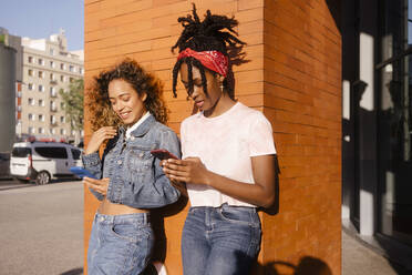 Young multiracial women using mobile phones in front of wall - MMPF00366