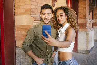 Lächelnde multirassische Freunde, die ein Selfie mit ihrem Mobiltelefon machen - MMPF00391