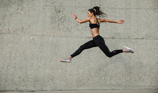 Weibliche Athletin beim Laufen und Springen, Seitenansicht einer flexiblen Athletin beim Training im Freien. - JLPSF07379