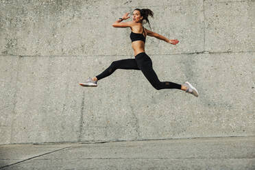 Sporty woman doing running and jumping exercise outdoors. Fitness female athlete exercising outdoors. - JLPSF07380