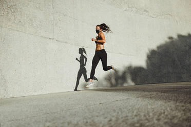 Athletic woman running outdoors wearing protective face mask. Female runner sprinting outdoors with a mask on. - JLPSF07394