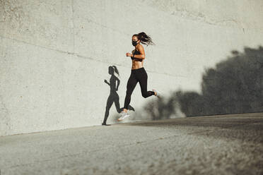 Sportliche Frau, die im Freien läuft und eine Gesichtsmaske trägt. Läuferin, die im Freien mit einer Maske sprintet. - JLPSF07394