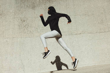 Woman in sportswear exercising outdoors. Woman running and jumping in sportswear. - JLPSF07436