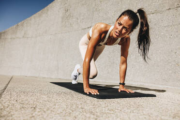 Healthy woman doing mountain climbers exercise. Female in sportswear exercising on a mat outdoors. - JLPSF07450