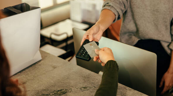 Unbekannter Kunde, der an der Kasse mit einer Kreditkarte bezahlt. Die Hand einer Frau, die eine Bankkarte auf ein kontaktloses Kreditkartenlesegerät legt. Frau, die in einem Bekleidungsgeschäft Kleidung kauft. - JLPSF07480