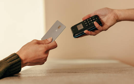 Eine Frau tippt mit der Hand eine Kreditkarte auf ein kontaktloses Kartenlesegerät. Eine nicht erkennbare Kundin bezahlt mit einer Kreditkarte an der Kasse. - JLPSF07484