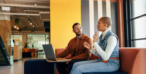 Zwei junge Geschäftsleute bei einer wichtigen Besprechung in einer Bürolobby. Zwei junge Unternehmer, die in einem Co-Working Space an einem neuen Projekt arbeiten. Moderne Geschäftsleute, die einen Laptop benutzen. - JLPSF07499