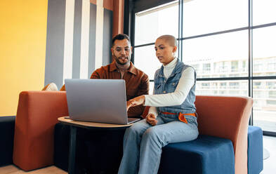 Junge Geschäftsleute bei einer wichtigen Besprechung in einer Bürolobby. Zwei Geschäftskollegen, die in einem modernen Co-Working Space einen Laptop benutzen. Zwei junge Unternehmer, die gemeinsam an einem neuen Projekt arbeiten. - JLPSF07500