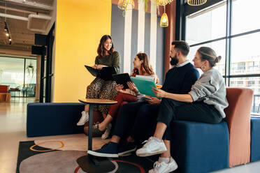 Group of multicultural businesspeople working in an office lobby. Team of young businesspeople smiling happily while sitting together in a co-working space. Entrepreneurs collaborating on a new project. - JLPSF07510