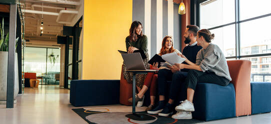 Multicultural businesspeople working in an office lobby. Group of happy businesspeople smiling while sitting together in a co-working space. Young entrepreneurs collaborating on a new project. - JLPSF07511