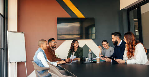 Glückliche Geschäftsleute bei einer Besprechung in einem Sitzungssaal. Eine Gruppe multiethnischer Geschäftsleute lächelt fröhlich während ihrer morgendlichen Besprechung. Junge Unternehmer arbeiten in einem modernen Büro zusammen. - JLPSF07513