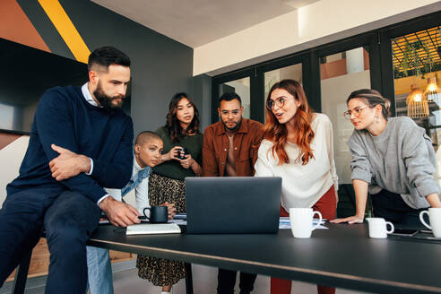 Gruppe von Geschäftsleuten bei einer Diskussion in einem Sitzungssaal. Gruppe von multikulturellen Geschäftsleuten, die in einem modernen Büro auf einen Laptop-Bildschirm schauen. Junge Unternehmer, die gemeinsam an einem neuen Projekt arbeiten. - JLPSF07524