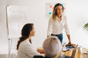 Young businesswoman leading a meeting in a boardroom. Happy young businesswoman sharing her ideas with her team. Group of multicultural businesswomen working together in an all-female startup. - JLPSF07544