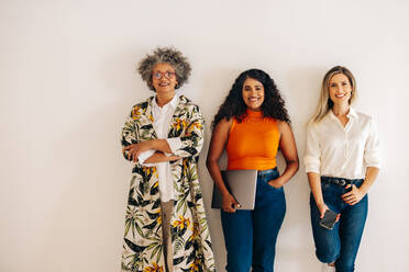 Three diverse businesswomen smiling at the camera while standing against an  office wall. Group of multicultural