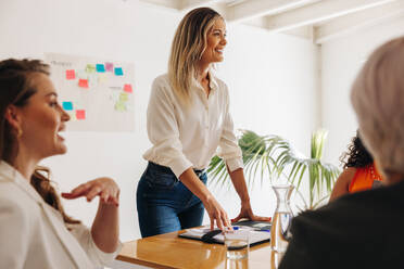 Junge Geschäftsfrau bei einer Besprechung mit ihrem Team. Zufriedene Teamleiterin beim Brainstorming mit ihren Kollegen in einem Sitzungssaal. Gruppe kreativer Geschäftsfrauen, die in einem reinen Frauen-Startup zusammenarbeiten. - JLPSF07603