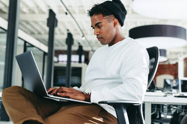 Software developer working on a new project in an office. Focused young businessman using a laptop while sitting in a modern workplace. Creative businessman working alone during the day. - JLPSF07625