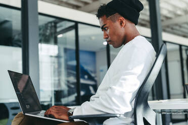 Creative businessman working on a new code in a modern office. Young software developer using a laptop while working on a new project. Focused young businessman sitting alone in a modern workplace. - JLPSF07628