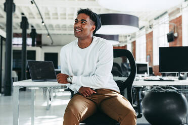 Happy software developer smiling in a modern office. Confident young businessman looking away while sitting alone. Young businessman taking a break while working on a new project. - JLPSF07630