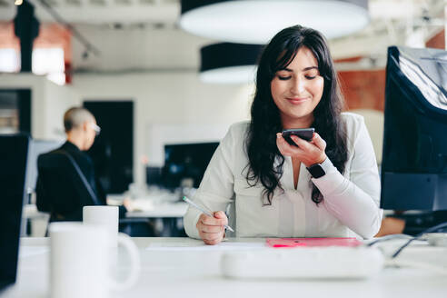 Kreative Geschäftsfrau beim Telefonieren im Büro. Glückliche junge Geschäftsfrau, die sich mit ihren Geschäftskunden in einem modernen Büro trifft. Junge Geschäftsfrau, die Geschäftspläne macht. - JLPSF07655